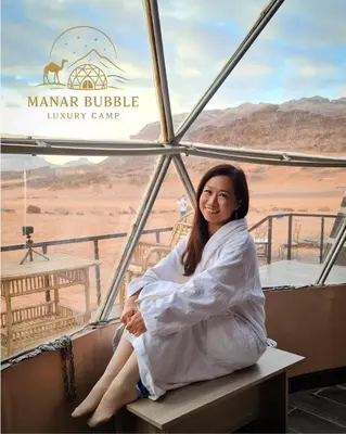 a woman sitting on a bench in the desert at Manar Bubbel Luxury Camp in Wadi Rum