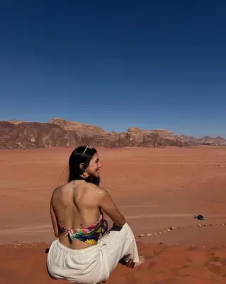 a woman sitting on the sand in the desert at MOON RUM lUXURY CAMP in Wadi Rum