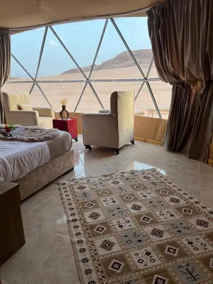 a bedroom with a bed and a chair and a large window at Royal Dunes Camp in Wadi Rum