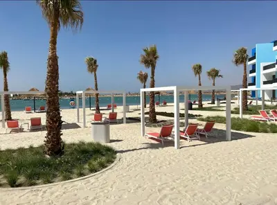 a beach with chairs and palm trees and the ocean at Ayla Apartment in Aqaba