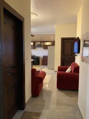a living room with two red couches and a kitchen at Cozy Flat, Amman Airport in Amman