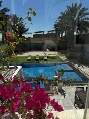 a swimming pool with pink flowers in the foreground at Maui Villa by Seahorse in Al Rama