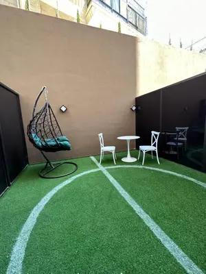 a green carpeted floor with chairs and a swing at Chic Apartments For Rent ave0-3 in Amman