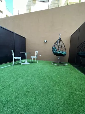 a room with green grass and two chairs and a table at Chic Apartments For Rent ave0-4 in Umm Uthainah