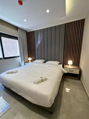 a bedroom with a large white bed with two lamps at Chic Apartments For Rent ave0-8 in Umm Uthainah