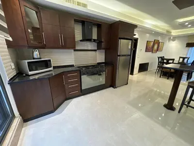 a kitchen with wooden cabinets and a microwave and a table at 2 En-suite Rooms, Central & Garden Terrace in Amman
