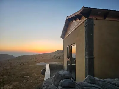 a house on a hill with the sunset in the background at Ramses Tafilah Lodge نزل رمسيس الطفيلة in At-Tafilah