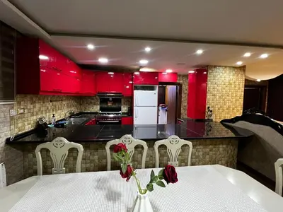 a kitchen with red cabinets and a white table and chairs at شقة للإجار في الجاردنز in ‘Urjān al Gharbīyah