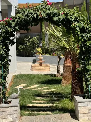a garden with an arch and a bird in the grass at شاليه بيت التل HILLHOUSE Chalet in Al Maşţabah