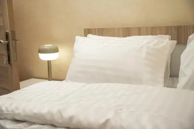 a white bed with a white pillow and a lamp at Hawari Group in Umm Uthainah