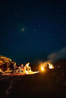 a group of people sitting around a campfire at night at Camp star road safari in Wadi Rum