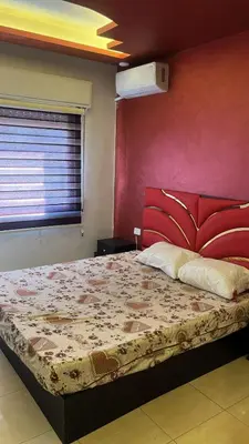 a bedroom with a large bed with a red wall at Izz AlDin Tamimi St شقة مفروش سوبر ديلوكس الجبيهة in Ţāb Kirā‘