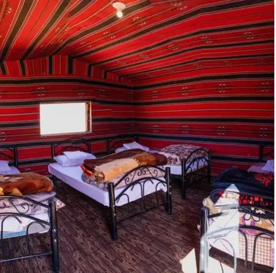 a room with three beds and a red wall at Wadi Rum Bedouin Story Camp & Tours in Wadi Rum