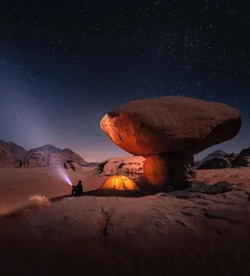 a person sitting in front of a mushroom in the desert at Wadi Rum Bedouin Story Camp & Tours in Wadi Rum