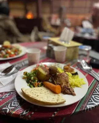 a plate of food with meat and vegetables on a table at Wadi Rum Bedouin Story Camp & Tours in Wadi Rum