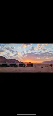 a sunset in the desert with buildings on a beach at Dream Bedouin Life Camp Wadi Rum in Disah