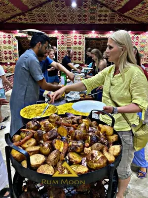 a woman is standing next to a grill with food at Rum Moon Camp in Wadi Rum