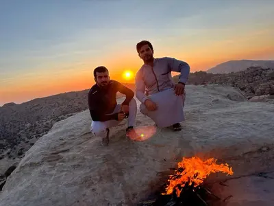 two men sitting on a rock next to a fire at Al -Nawatef Eco Lodge- Dana Nature Reserve in Dana