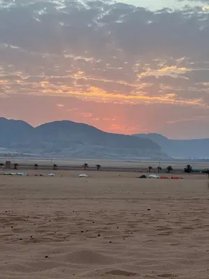a beach with mountains in the background and a sunset at Ayman camp in Wadi Rum