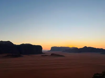 a sunset over the desert with mountains in the background at Emad wadi rum camp in Wadi Rum