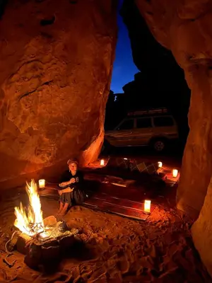 a person sitting next to a fire in a cave at Emad wadi rum camp in Wadi Rum