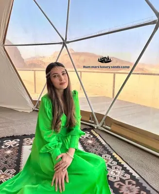 a woman in a green dress sitting under an umbrella at RUM MARS lUXURY SANDS BUBBLE CAMP in Wadi Rum