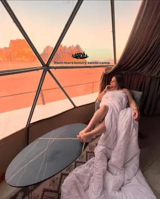 a man laying in bed talking on a cell phone at RUM MARS lUXURY SANDS BUBBLE CAMP in Wadi Rum