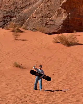 a man holding a surfboard in the desert at Desert Magic Camp in Wadi Rum