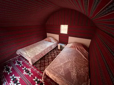 two beds in a room with red walls at Desert Rock Wadi Rum in Wadi Rum