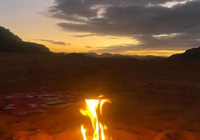 a fire burns in the desert at sunset at Desert Waves Camp in Wadi Rum