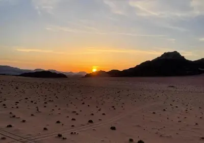 a sunset in the desert with rocks in the sand at Desert Waves Camp in Wadi Rum