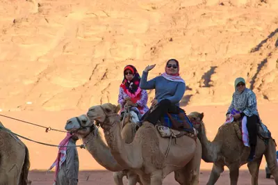 three people riding on the camels in the desert at Panorama Wadi Rum Sunset Camp in Wadi Rum