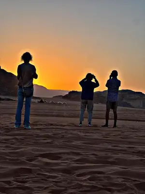 three people standing in the desert watching the sunset at CAPITAL RUM lUXURY CAMP in Wadi Rum