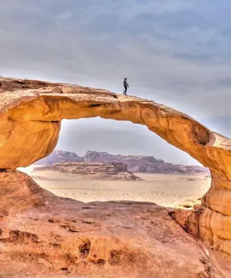 a man standing on top of an arch in the desert at CAPITAL RUM lUXURY CAMP in Wadi Rum