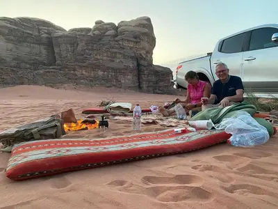 a man and a woman sitting in the sand next to a large object at Bedouin house in Wadi Rum