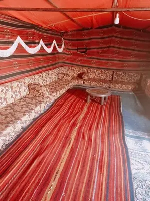 a room with a long red wall with a table at Wadi Ghowair View Camp in Al Khuraybah
