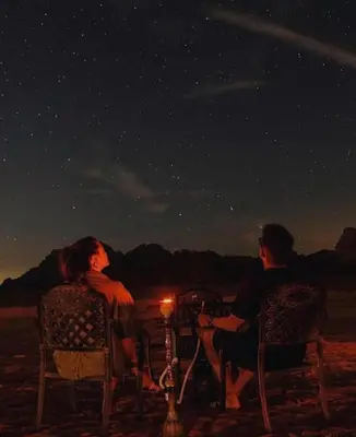 a man and woman sitting at a table under the stars at مخيم وهج رم in Disah