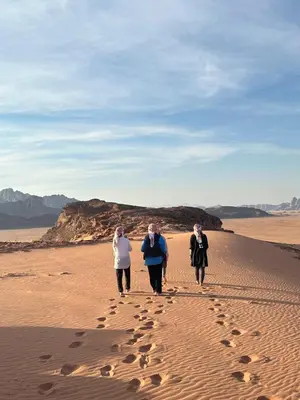 three people walking in the desert with footprints in the sand at Rum drone tours in Aqaba