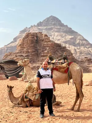 a man standing next to a camel and the pyramids at Rum drone tours in Aqaba