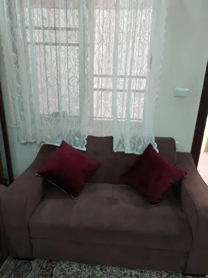 a brown couch with two pillows in front of a window at Nice comfy room in Amman