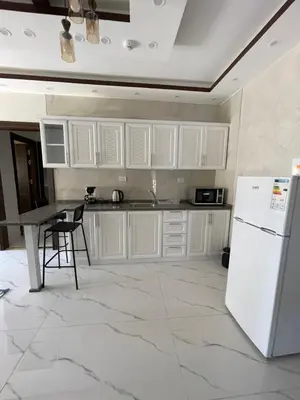 a kitchen with white cabinets and a table and a refrigerator at Sawa Apartment in Amman