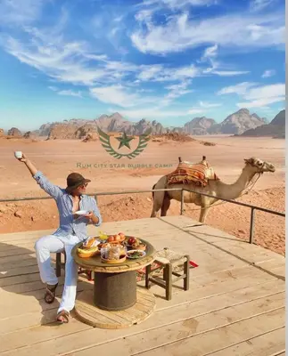 a woman sitting on a table in the desert with a camel at RUM CITY STAR BUBBLE lUXURY CAMP in Wadi Rum