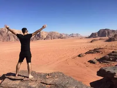 a man standing on a rock in the desert at Wadi Rum 5-hour tour with sunset or morning, overnight stay with two meals and a Bedouin tent with a private bathroom Prices are for two people in Wadi Rum