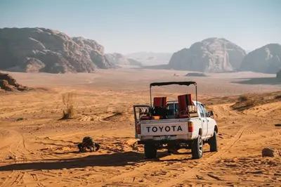 a white toyota truck driving through the desert at Wadi Rum 5-hour tour with sunset or morning, overnight stay with two meals and a Bedouin tent with a private bathroom Prices are for two people in Wadi Rum