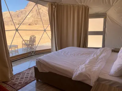 a bedroom with a bed and a large window at Al Jawhara Luxury Camp in Wadi Rum