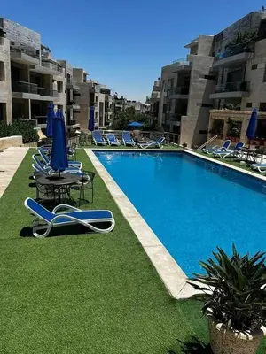 a swimming pool with lawn chairs and blue umbrellas at Luxury home Abdoun complex in Amman