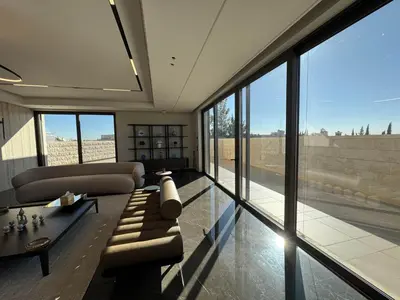 a living room with a couch and a table and windows at Dabouq Luxurious Penthouse in Amman