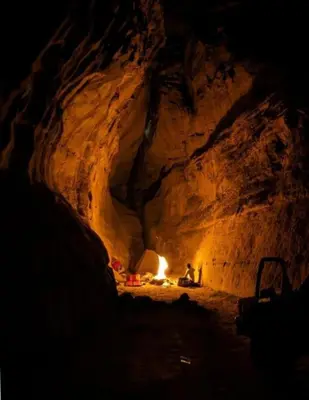 a person sitting in a cave with a fire in it at Wadi Rum sleeping in the desert in Wadi Rum