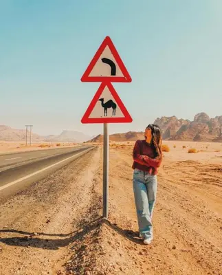 a woman standing next to a sign on the side of a road at Wadi Rum sleeping in the desert in Wadi Rum