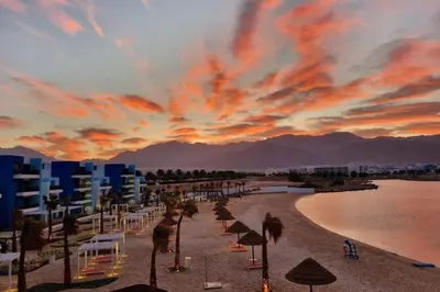 a beach with chairs and umbrellas at sunset at Azure haven Ayla Sea view Apartment in Aqaba